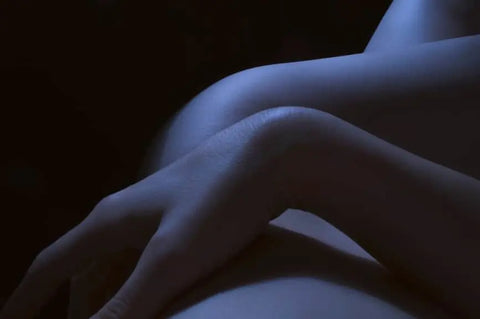 Naked woman lying with crossed arms under blue light, symbolizing blue light skin protection
