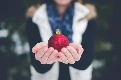 Person holding a red festive ornament, symbolizing holiday skincare care
