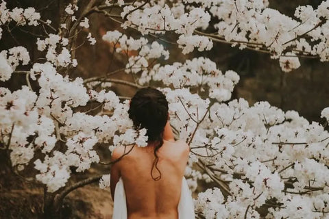 Woman with bare back in front of blooming flowers, symbolizing spring skincare renewal