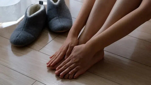 Woman’s hands and feet near slippers, symbolizing winter skincare and dryness
